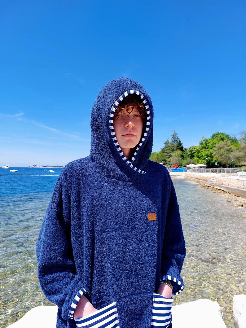 May include: A navy blue hooded towel with white stripes on the hood and pockets. The towel has a brown patch with the word "ONE" on it.