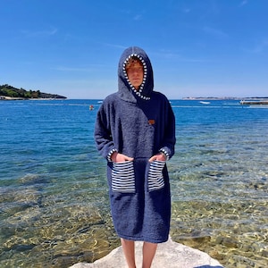 May include: A navy blue hooded towel robe with white stripes on the pockets. The robe is made of a soft, absorbent material and is perfect for drying off after a swim.