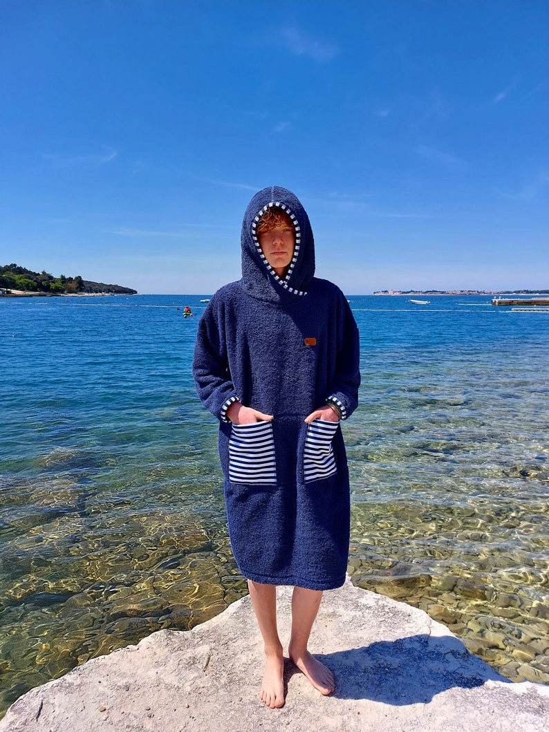 May include: A navy blue hooded towel robe with white stripes on the pockets. The robe is made of a soft, absorbent material and is perfect for drying off after a swim.