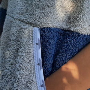 May include: A gray and blue hooded towel with a white and gray geometric pattern on the side. The towel is made of soft, fluffy material.