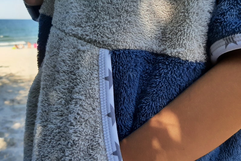 May include: A gray and blue hooded towel with a white and gray geometric pattern on the side. The towel is made of soft, fluffy material.