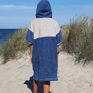 May include: A person wearing a blue and gray hooded towel robe on a sandy beach.