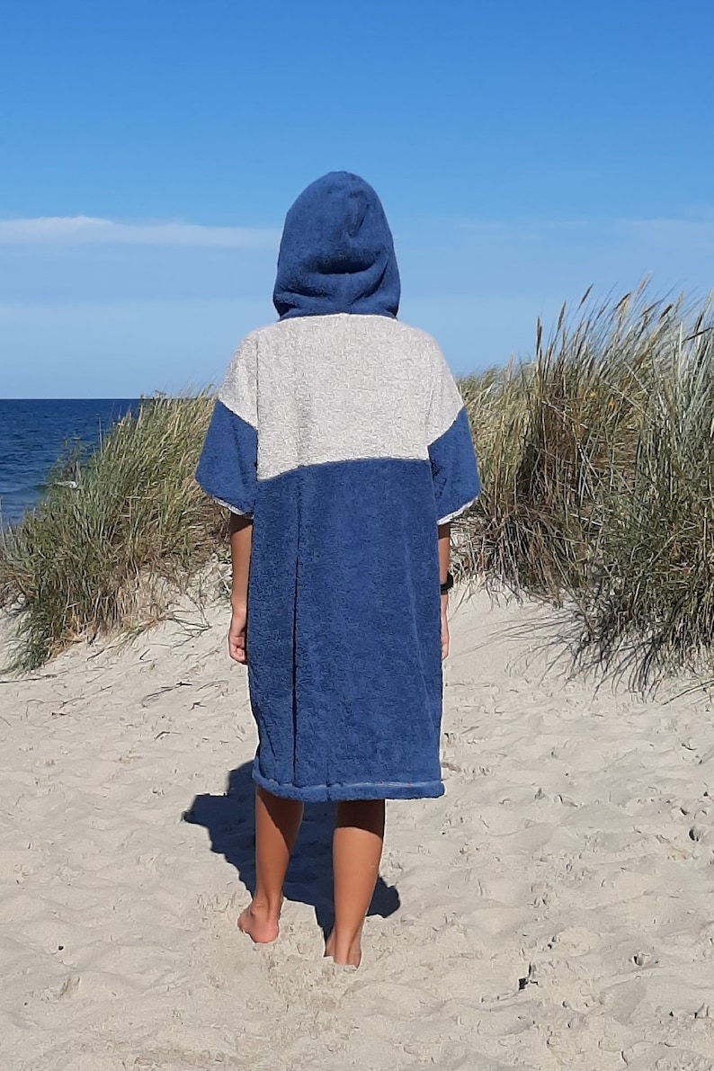 May include: A person wearing a blue and gray hooded towel robe on a sandy beach.