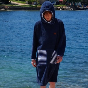 May include: A dark blue hooded towel with white stripes on the pocket. The towel is made of a soft, absorbent material and is perfect for drying off after a swim or shower.