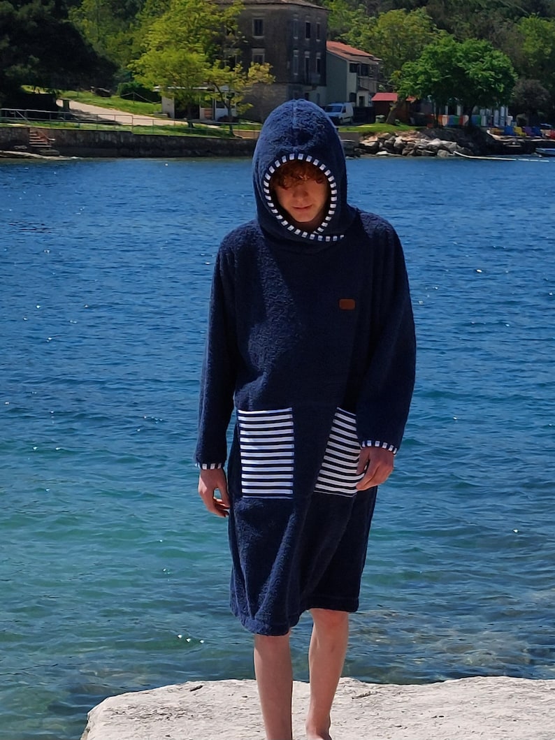 May include: A dark blue hooded towel with white stripes on the pocket. The towel is made of a soft, absorbent material and is perfect for drying off after a swim or shower.