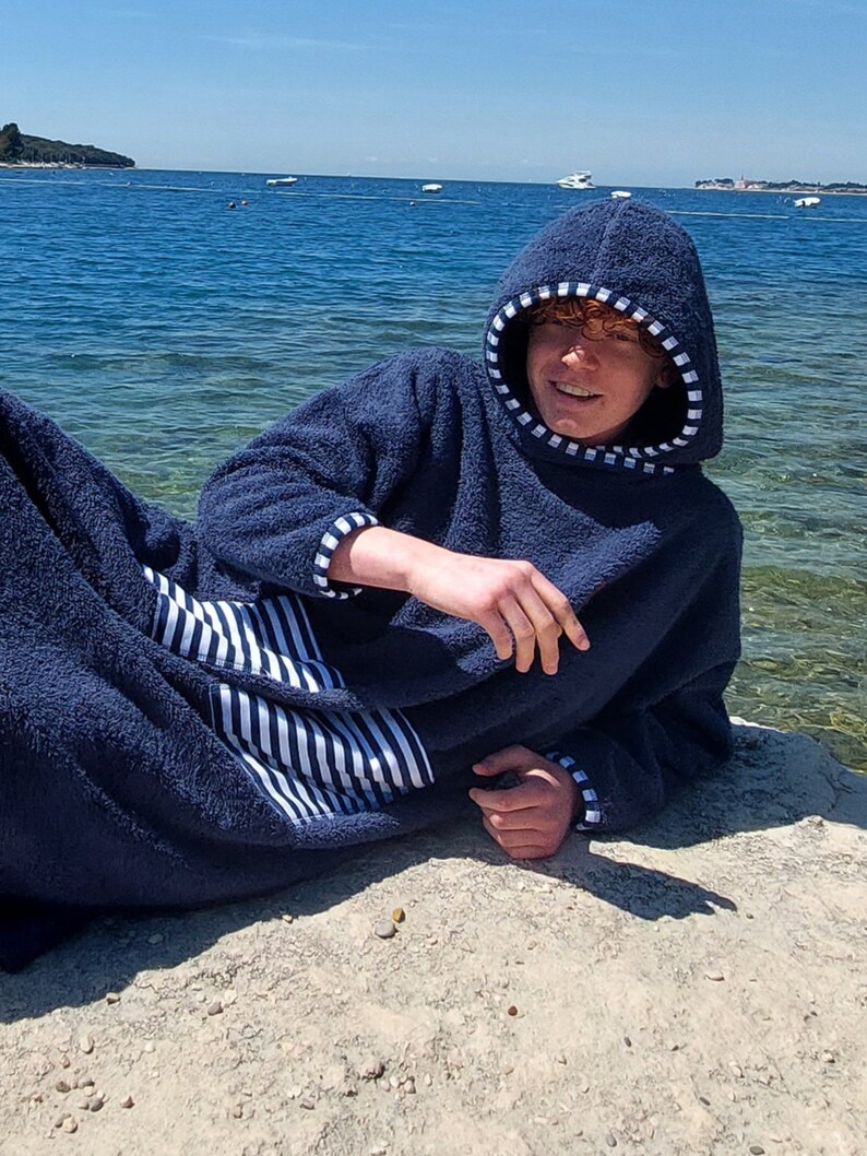 May include: A navy blue hooded towel robe with white stripes on the pocket and trim. The robe is made of soft, absorbent material and is perfect for drying off after a swim.