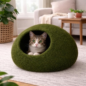 Peut inclure: Une grotte pour chat en feutre vert olive fonc&eacute;, en forme de d&ocirc;me avec une ouverture circulaire. Un chat tigr&eacute; brun aux yeux verts et aux marques blanches sur le visage et la poitrine repose &agrave; l'int&eacute;rieur, regardant droit devant lui.
