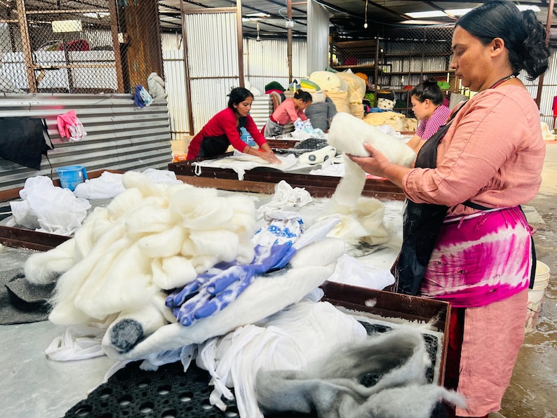 Peut inclure: Une collection de fibres de laine blanche brute et de morceaux de tissu teints en bleu, empil&eacute;s sur une table en m&eacute;tal. La laine est duveteuse et non fil&eacute;e, tandis que les morceaux de tissu pr&eacute;sentent un motif bleu et blanc distinct.