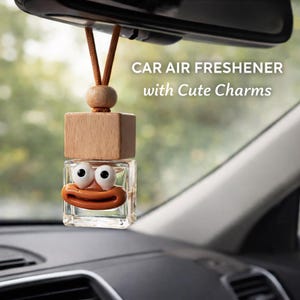 May include: A car air freshener with a cute charm design. The clear glass bottle has a cartoon face with large white eyes and an orange mouth. The freshener hangs from a wooden block and a brown string, with the text "CAR AIR FRESHENER with Cute Charms".