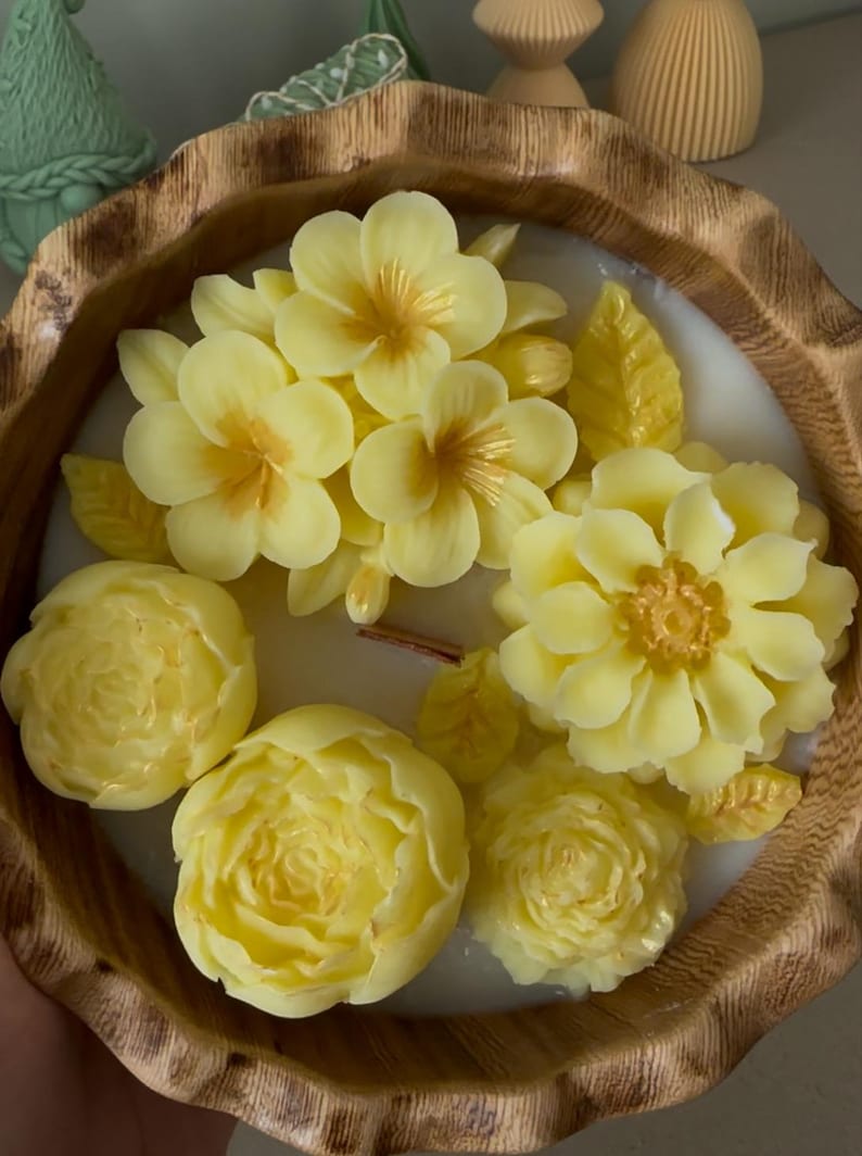 May include: A yellow floral candle in a wooden bowl. The candle features a variety of yellow flowers, including roses, peonies, and plumeria.