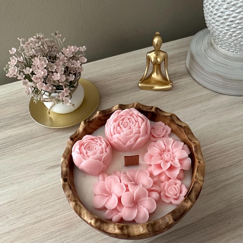 May include: A wooden bowl filled with a pink floral scented candle. The candle is shaped like a bouquet of flowers and has a natural wood wick.