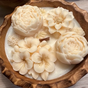 May include: A white candle in a wooden bowl with a floral design. The candle is decorated with white flowers and gold accents.
