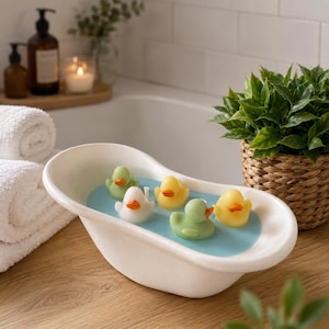 May include: A white ceramic miniature bathtub filled with light blue liquid and five small rubber ducks in yellow, white, and light green. Each duck features a distinct orange beak. The miniature tub is shaped like a classic clawfoot basin.