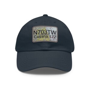 May include: Navy blue baseball cap with a rectangular patch featuring the text "N703TW Cessna 172" over a map design. The cap is made of a soft material and has a curved brim.