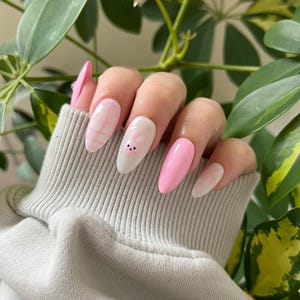 Puede incluir: U&ntilde;as postizas ovaladas de color rosa y blanco con un dise&ntilde;o a cuadros rosa y blanco, una u&ntilde;a blanca con una carita de conejo rosa y una u&ntilde;a rosa s&oacute;lida.