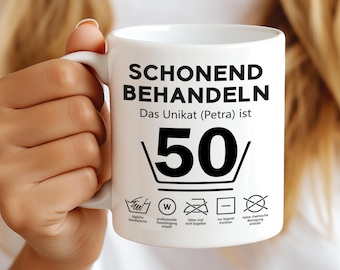 May include: White ceramic mug with black text that reads "Schonend Behandeln Das Unikat (Petra) ist 50".  The mug has a black and white graphic of a washing instruction symbol with the number 50 inside.  The mug also has five black and white washing instruction symbols.