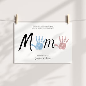 Puede incluir: Impresi&oacute;n blanca con la palabra "Mum" en escritura negra, con huellas de manos azules y rosas que reemplazan las "u". La impresi&oacute;n incluye el texto "&iexcl;Para el mundo eres nuestra mam&aacute;, pero para nosotros eres todo el mundo!" y "Te queremos, Sophia & Jonas."