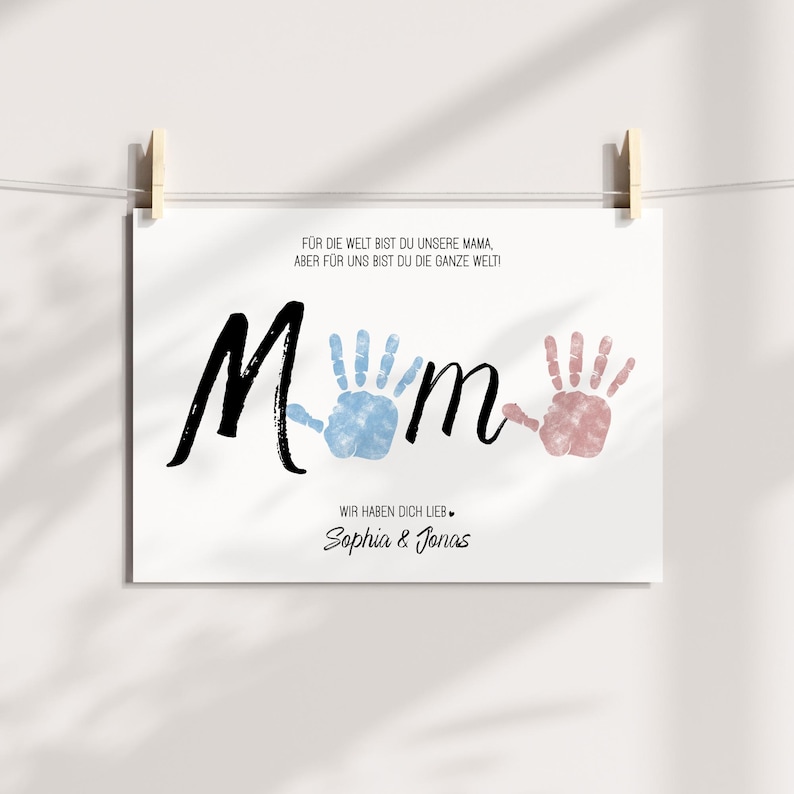 Puede incluir: Impresi&oacute;n blanca con la palabra "Mum" en escritura negra, con huellas de manos azules y rosas que reemplazan las "u". La impresi&oacute;n incluye el texto "&iexcl;Para el mundo eres nuestra mam&aacute;, pero para nosotros eres todo el mundo!" y "Te queremos, Sophia & Jonas."