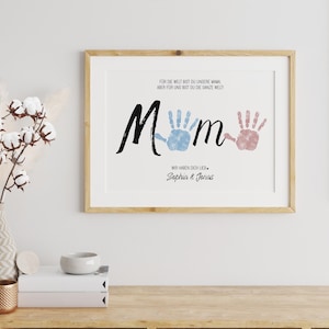 Puede incluir: Impresi&oacute;n enmarcada con la palabra "Mom" en escritura negra, huellas de manos azules y rosas, y el texto: "Para el mundo eres nuestra mam&aacute;, pero para nosotros eres el mundo entero! Te queremos. Sophia & Jonas."