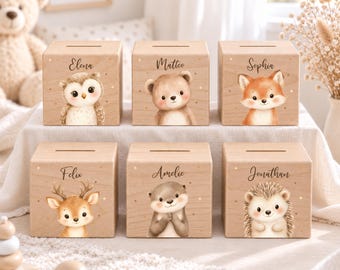 May include: Six light-colored wooden cube-shaped money boxes, each featuring a unique animal illustration and a name printed in black script. The animals include an owl, bear, fox, deer, otter, and hedgehog, all accented with small gold dots.