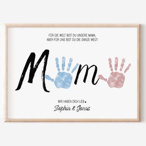 Puede incluir: Una impresi&oacute;n enmarcada con la palabra "Mom" en escritura negra, con huellas de manos azules y rosas. La impresi&oacute;n incluye texto en alem&aacute;n y los nombres "Sophia & Jonas" en cursiva, todo sobre un fondo blanco.