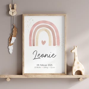 Peut inclure: Une impression d'arc-en-ciel aquarelle avec un sch&eacute;ma de couleurs rose, beige et marron. L'arc-en-ciel a un petit c&oelig;ur au centre. L'impression comprend le nom "Leonie", la date "09. Februar 2025" et l'heure "22:18 Uhr" ainsi que le poids "3315 g" et la longueur "52 cm".