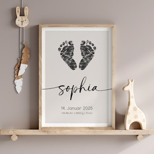 Peut inclure: Une impression encadr&eacute;e avec des empreintes de pieds d'encre noire en forme de c&oelig;ur. Le nom "Sophia" est &eacute;crit en cursive sous les empreintes de pieds. La date "14. Januar 2025" et l'heure "09:48 Uhr | 3650g | 51cm" sont imprim&eacute;es sous le nom.