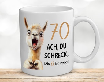 May include: White ceramic mug with a cartoon llama and the text "70 ACH, DU SCHRECK, Die 6 ist weg!"