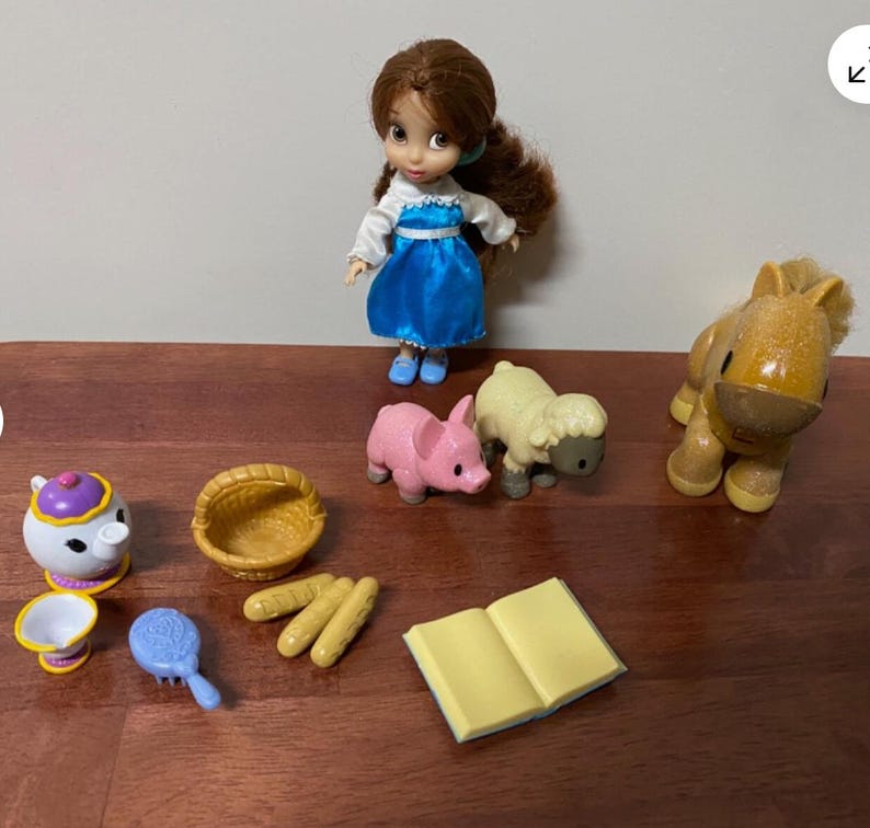 Pode incluir: Uma cole&ccedil;&atilde;o de miniaturas de brinquedos e acess&oacute;rios, incluindo uma boneca com um vestido azul, um porco rosa, uma ovelha amarela, um cavalo, uma chaleira, uma cesta, p&atilde;o, uma escova de cabelo e um livro aberto. Os brinquedos est&atilde;o dispostos numa superf&iacute;cie de madeira.