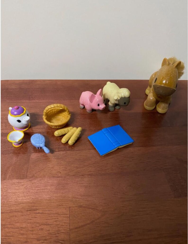 Pode incluir: Uma cole&ccedil;&atilde;o de pequenas figuras de brinquedo e acess&oacute;rios coloridos. Inclui um porco rosa, uma ovelha amarela, um cavalo castanho, uma chaleira branca com tampa roxa, uma cesta amarela, um livro azul, uma escova azul e p&atilde;o amarelo.