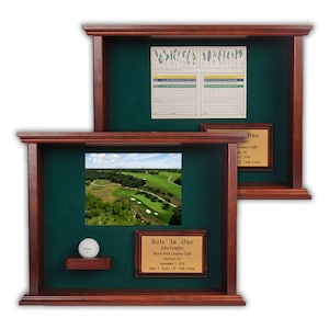 May include: Two wooden display cases with a green felt backing. One case features a golf ball, a photo of a golf course, and a plaque that reads "Hole In One." The other case has a scorecard and a plaque.