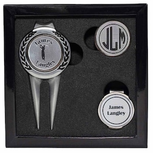 May include: A golf gift set in a black box. The set includes a divot repair tool with "James Langley" and a golfer silhouette, a ball marker with "JLM" initials, and a magnetic ball marker with "James Langley".
