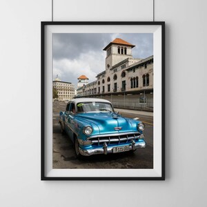 May include: A vintage blue car with a white roof is parked on a street in front of a building with a red tile roof. The car has a license plate that reads "P 115 080".