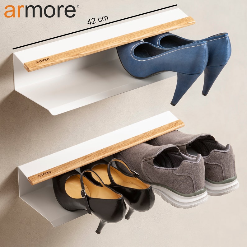 Op de afbeelding: Twee witte, aan de muur gemonteerde schoenenrekken met houten rails. De bovenste plank heeft een paar blauwe hakken en de onderste plank heeft een paar zwarte hakken en een paar grijze sneakers. De planken zijn 42 cm breed.