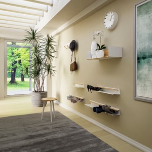 Op de afbeelding: Witte wandbevestigde schoenenrekken met houten accenten, met een set van drie planken met een paar schoenen op elke plank. Een witte klok hangt aan de muur boven de planken.