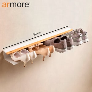Op de afbeelding: Een wit, aan de muur gemonteerd schoenenrek met een houten plank en een label met de tekst "armore". Het rek is 80 cm lang en biedt ruimte voor zes paar schoenen, waaronder hakken en sneakers.