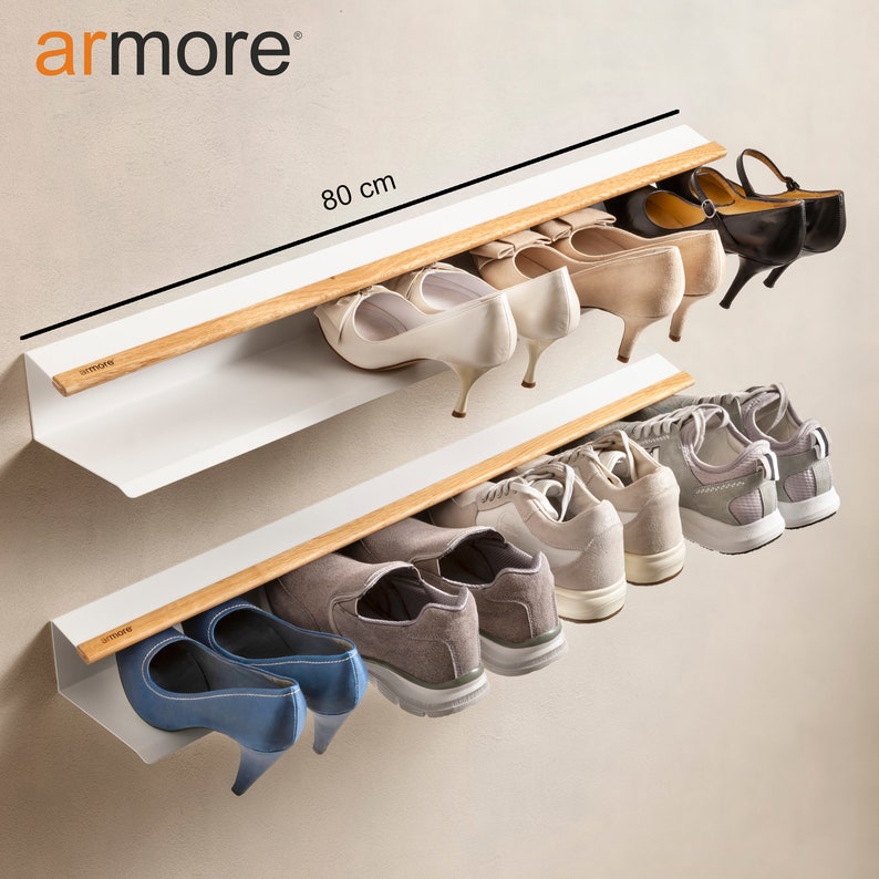 Op de afbeelding: Een wit, aan de muur gemonteerd schoenenrek met twee planken en houten rails. Het rek is 80 cm breed en biedt ruimte voor verschillende soorten schoenen, waaronder sneakers, hakken en ballerina's.