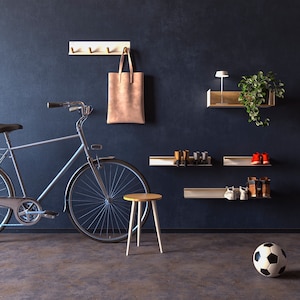 Op de afbeelding: Een grijze fiets met een bruine leren tas die aan een witte haak hangt. Er zijn drie witte planken met schoenen erop. Een witte kruk en een voetbal liggen op de vloer.