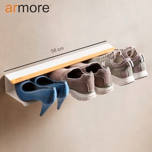 Op de afbeelding: Een wit, aan de muur gemonteerd schoenenrek met een bamboe plank. Het rek is 58 cm lang en biedt ruimte voor vier paar schoenen, waaronder twee paar sneakers en twee paar hakken.
