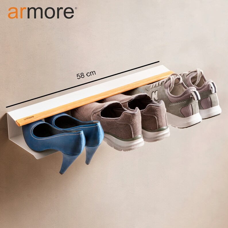 Op de afbeelding: Een wit, aan de muur gemonteerd schoenenrek met een bamboe plank. Het rek is 58 cm lang en biedt ruimte voor vier paar schoenen, waaronder twee paar sneakers en twee paar hakken.
