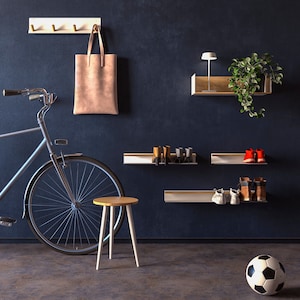 Op de afbeelding: Een blauwe fiets met een bruine leren tas die aan een witte haakrek hangt. De muur is donkerblauw en er zijn drie witte planken met verschillende schoenen en een lamp op een van de planken. Een kleine houten kruk staat voor de fiets.