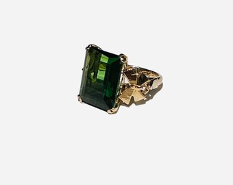 Può includere: Un anello d'oro con una grande pietra preziosa verde smeraldo incastonata a griffe.