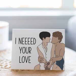 May include: A white card with black text that reads "I NEEEED YOUR LOVE" and a cartoon illustration of two people hugging.