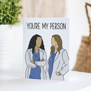 May include: A white card with the text "YOU'RE MY PERSON" in black lettering. Two cartoon figures of women wearing white coats and blue scrubs are depicted on the card.