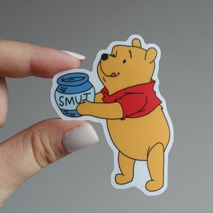 May include: A Winnie the Pooh cartoon character sticker holding a blue jar with the word "SMUT" written on it.