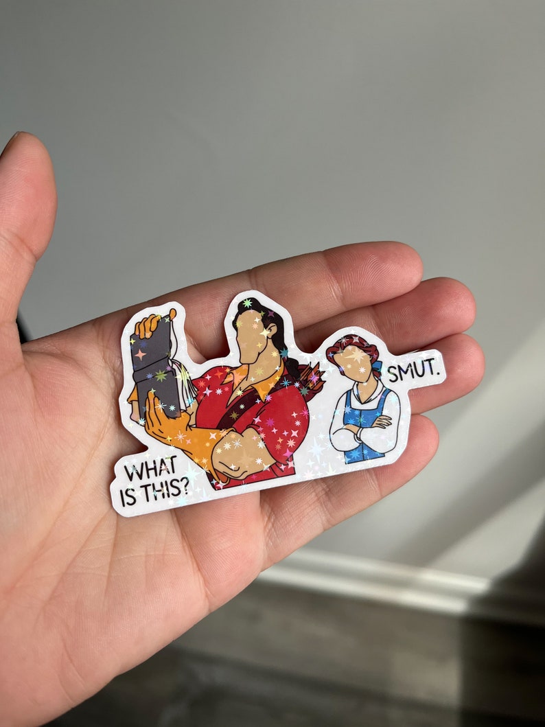 K&ouml;nnte beinhalten: Ein Aufkleber mit einer Cartoon-Illustration von Belle und dem Biest aus dem Disney-Film Die Sch&ouml;ne und das Biest. Das Biest h&auml;lt ein Buch und Belle steht mit verschr&auml;nkten Armen da. Der Text "What is this?" befindet sich unter dem Biest und der Text "Smut." &uuml;ber Belle.