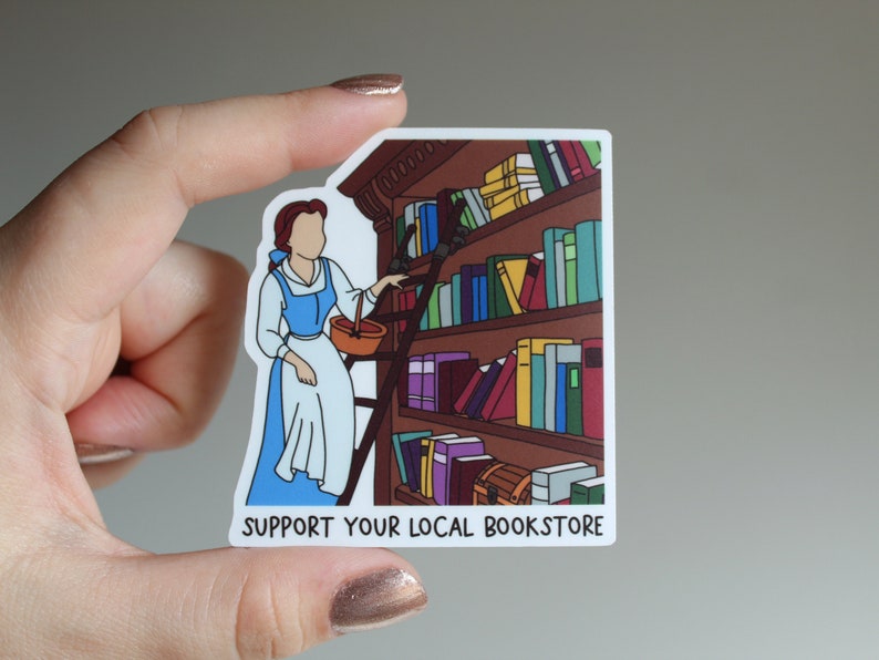 May include: A sticker featuring a cartoon illustration of Belle from Beauty and the Beast reaching for a book on a bookshelf. The sticker has the text "SUPPORT YOUR LOCAL BOOKSTORE" at the bottom.