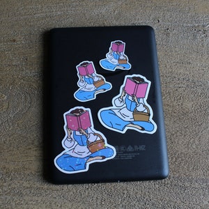 May include: Four stickers featuring a cartoon illustration of a person reading a book. The person is wearing a blue dress and a white apron. The stickers are on a black background.