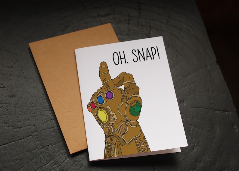 May include: A white card with a gold hand wearing a gauntlet with colorful gems. The text "OH. SNAP!" is written in black at the top of the card.