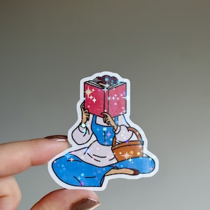 May include: A sticker of a cartoon woman reading a book with a basket in her hand. The sticker has a sparkly, iridescent finish.